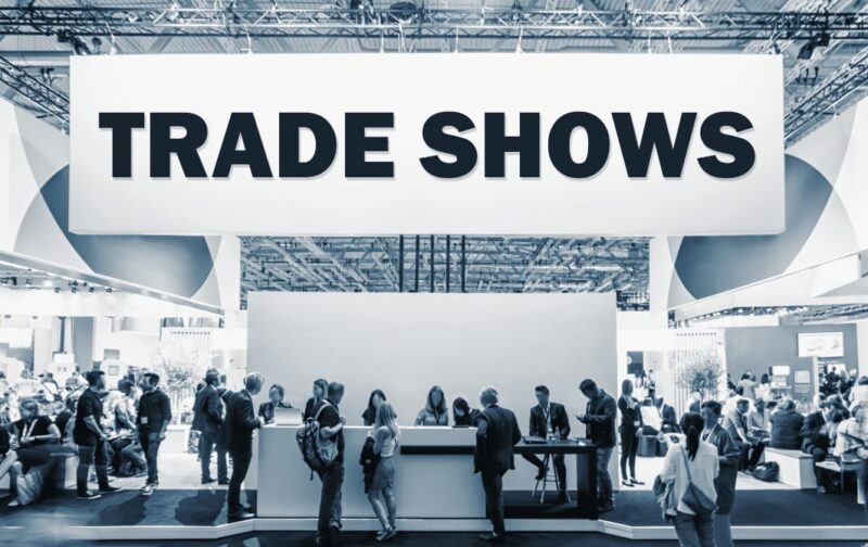 Adobe Stock royalty-free image #245272073, 'Crowd of people at a trade show booth with a banner and the text Trade Shows.' uploaded by rcfotostock, standard license purchased from https://stock.adobe.com/images/download/245272073; file retrieved on May 25th, 2019. License details available at https://stock.adobe.com/license-terms - image is licensed under the Adobe Stock Standard License