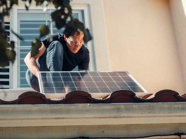 Photo by Kindel Media: https://www.pexels.com/photo/a-man-in-black-shirt-installing-a-solar-panel-on-the-roof-9875405/